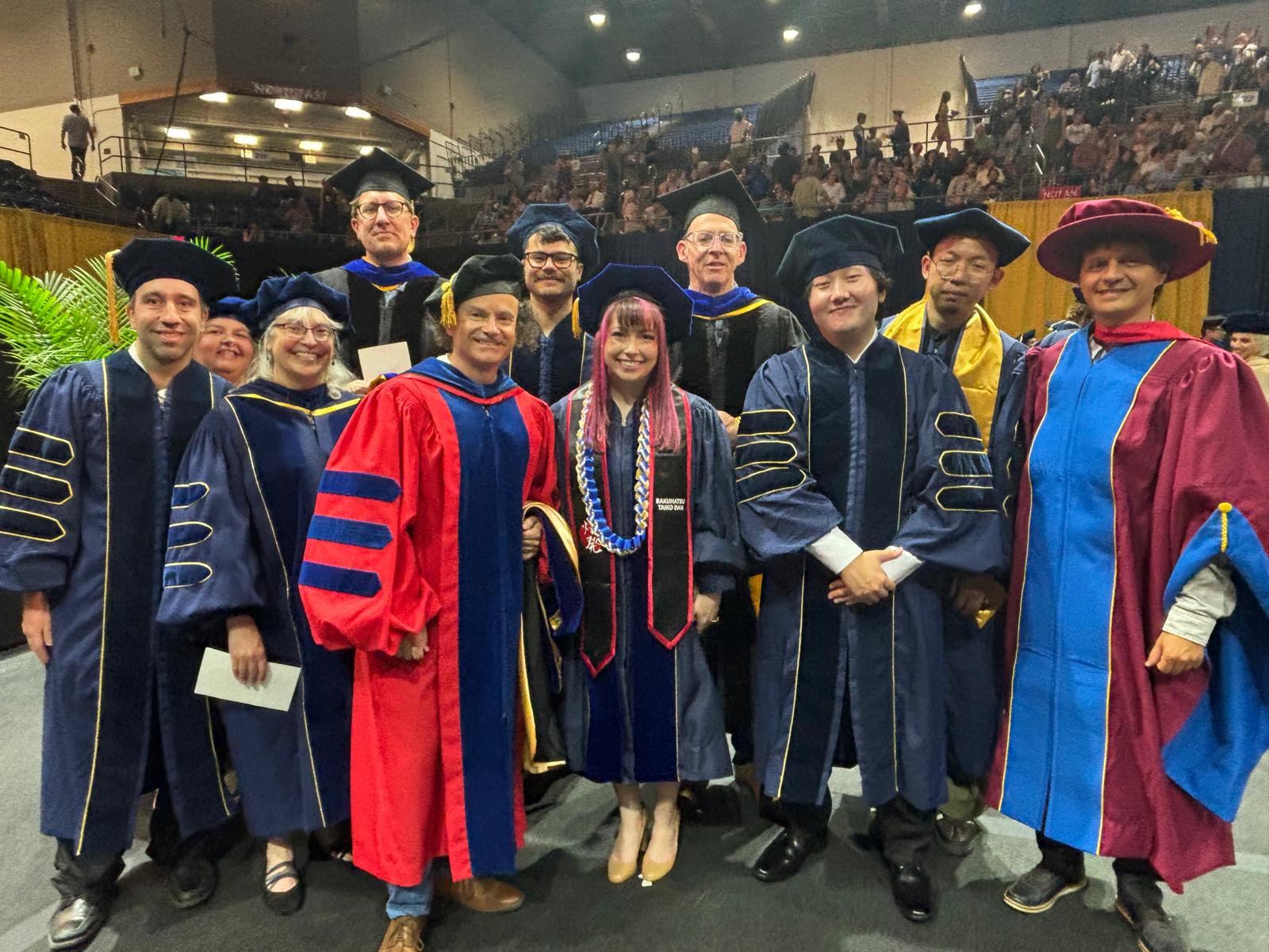 A group of academic robed students and faculty in robes that represent their alma mater or UC Davis, with deep blue and gold for UC Davis, 
