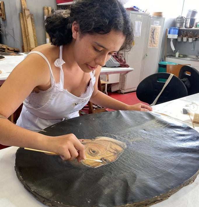 Young woman focused on restoring a face on a round black canvas in a workshop