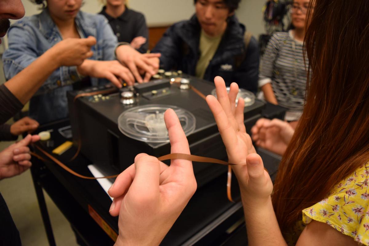 Photo of several people's hands manipulating magnetic tape in a large studio space