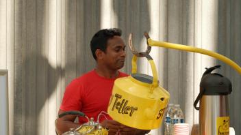 Man in red shirt behind yellow coffee cart with vintage percolator and thermos