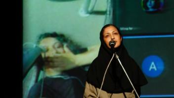 Woman in black hijab singing into microphone with large projected photo behind