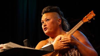 Performer in sequined dress holding ukulele, expressive face on dark stage