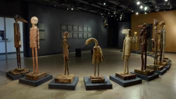 Museum gallery with tall wooden carved humanoid figures on pedestals under dim lighting