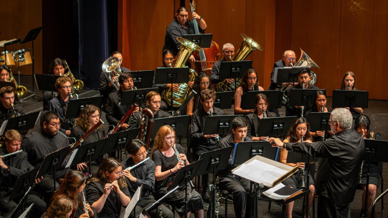 Conductor leading a band on a warm wood-paneled concert stage