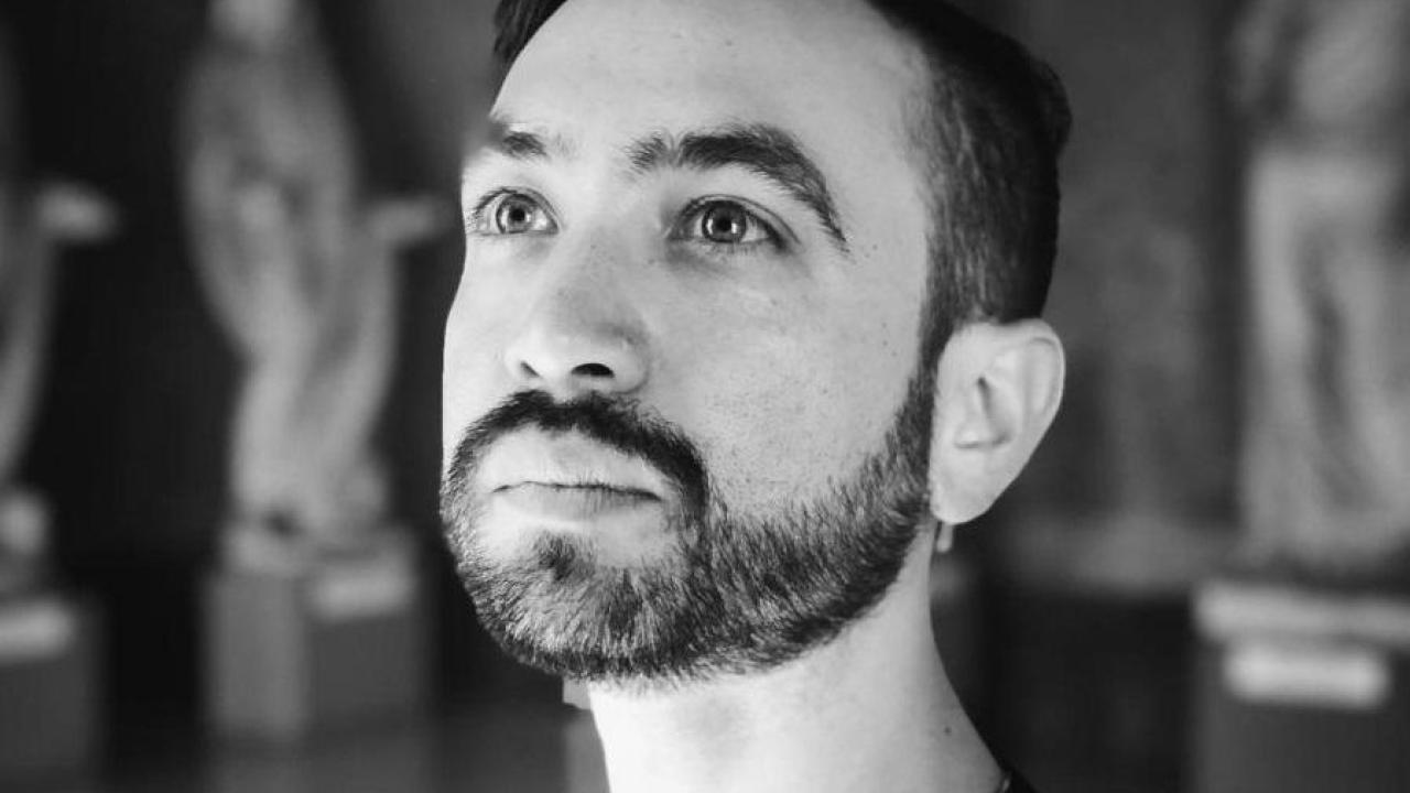 Black-and-white portrait of Alex van Gils, bearded, looking off to the side with classical statues visible in the background.
