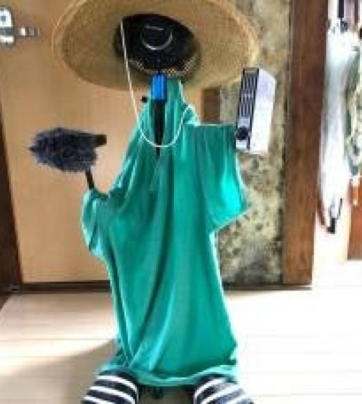 Clothes-stuffed mannequin wearing straw hat and green shirt, holding fuzzy mic and recorder