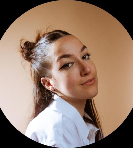 Headshot photo of young woman with half-up bun, slight smile, beige background.