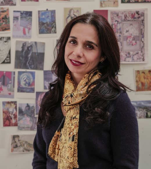 Smiling woman with yellow scarf standing before a colorful art-filled wall (photo)