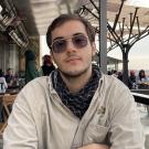 Young man with sunglasses and black scarf seated at outdoor café, neutral expression