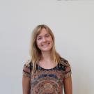 Smiling blonde woman in patterned top standing against a plain light wall