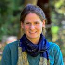 Outdoor portrait of smiling woman with a lapis lazuli blue scarf, teal button up shirt, blurred green forest background
