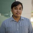 Portrait of Josiah Catalan wearing a blue plaid shirt in an indoor classroom-like setting.