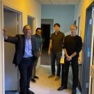 Four researchers walking together down a softly lit hallway with pale blue and yellow walls.