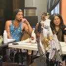 Two people seated at a table, attentive, with a large falcon perched on the table