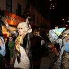 Masked revelers in ornate costumes march down a nighttime city street