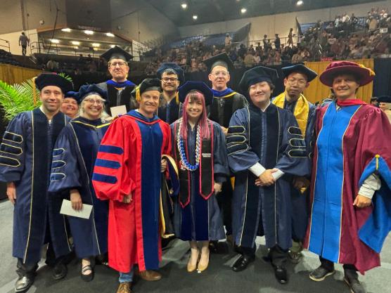 A group of academic robed students and faculty in robes that represent their alma mater or UC Davis, with deep blue and gold for UC Davis, 