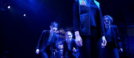 Four actors dressed in black on thrust stage