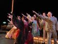Actors in colorful costumes point upwards toward the audience.